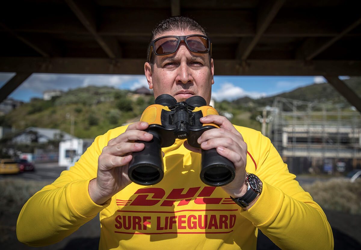 DR JONATHON WEBBER. IMAGE CREDIT MICHAEL CRAIG NEW ZEALAND, Surf Lifeguard mit Fernglas und Sonnenbrille.
