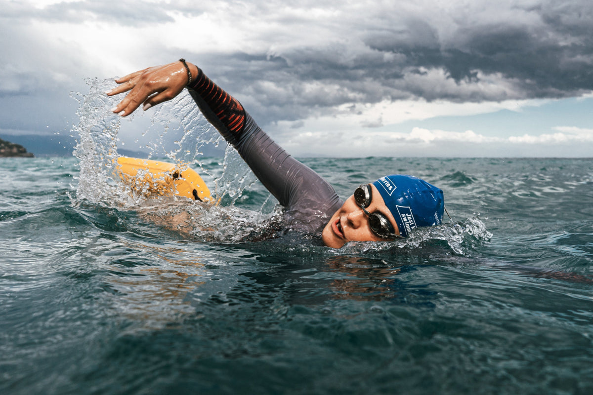 Open water swimmer Nathalie Pohl swimming freestyle in choppy sea under dark storm clouds, with a yellow RESTUBE buoy behind her