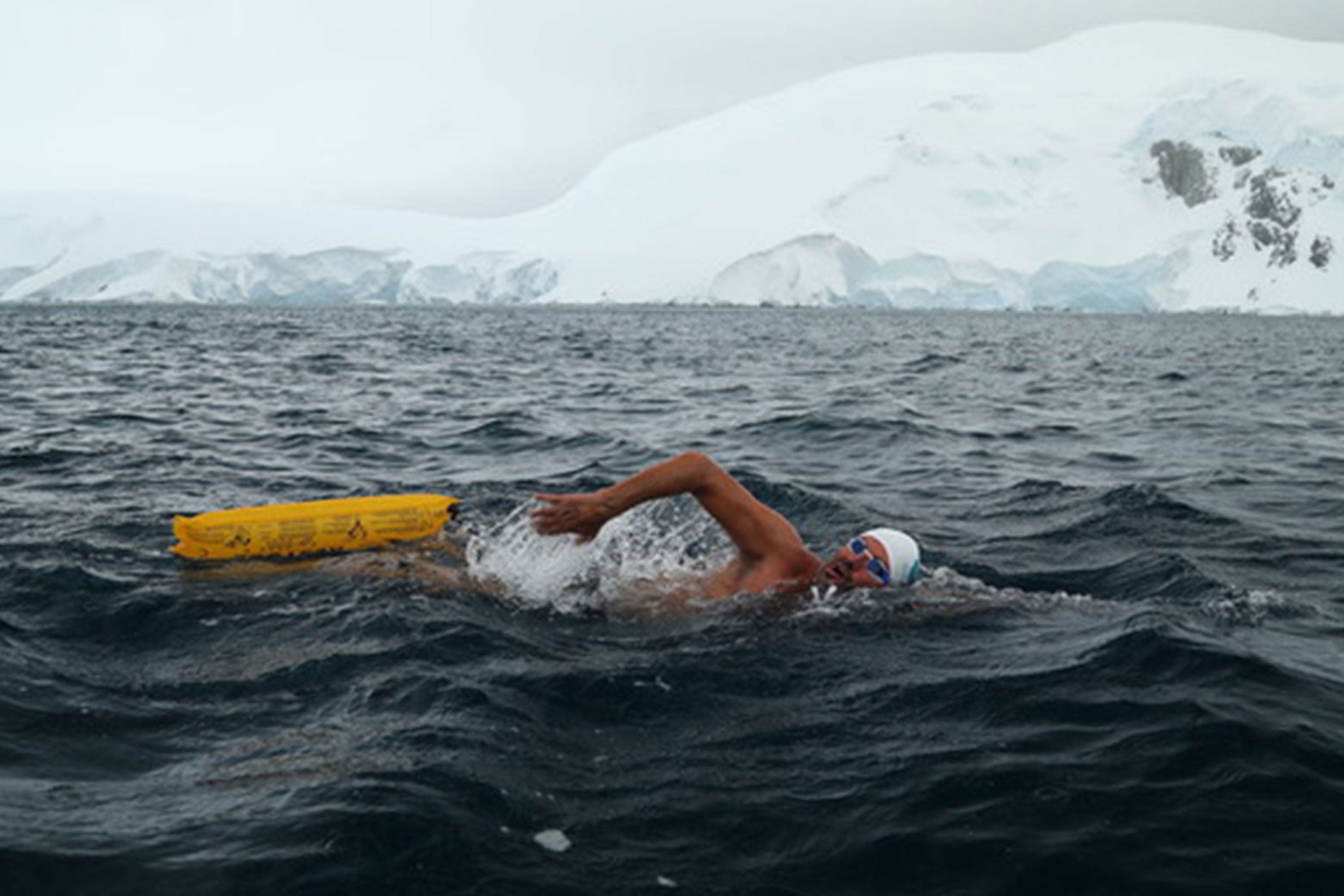 A swimmer with yellow RESTUBE buoy in icy water in front of a cruise ship.