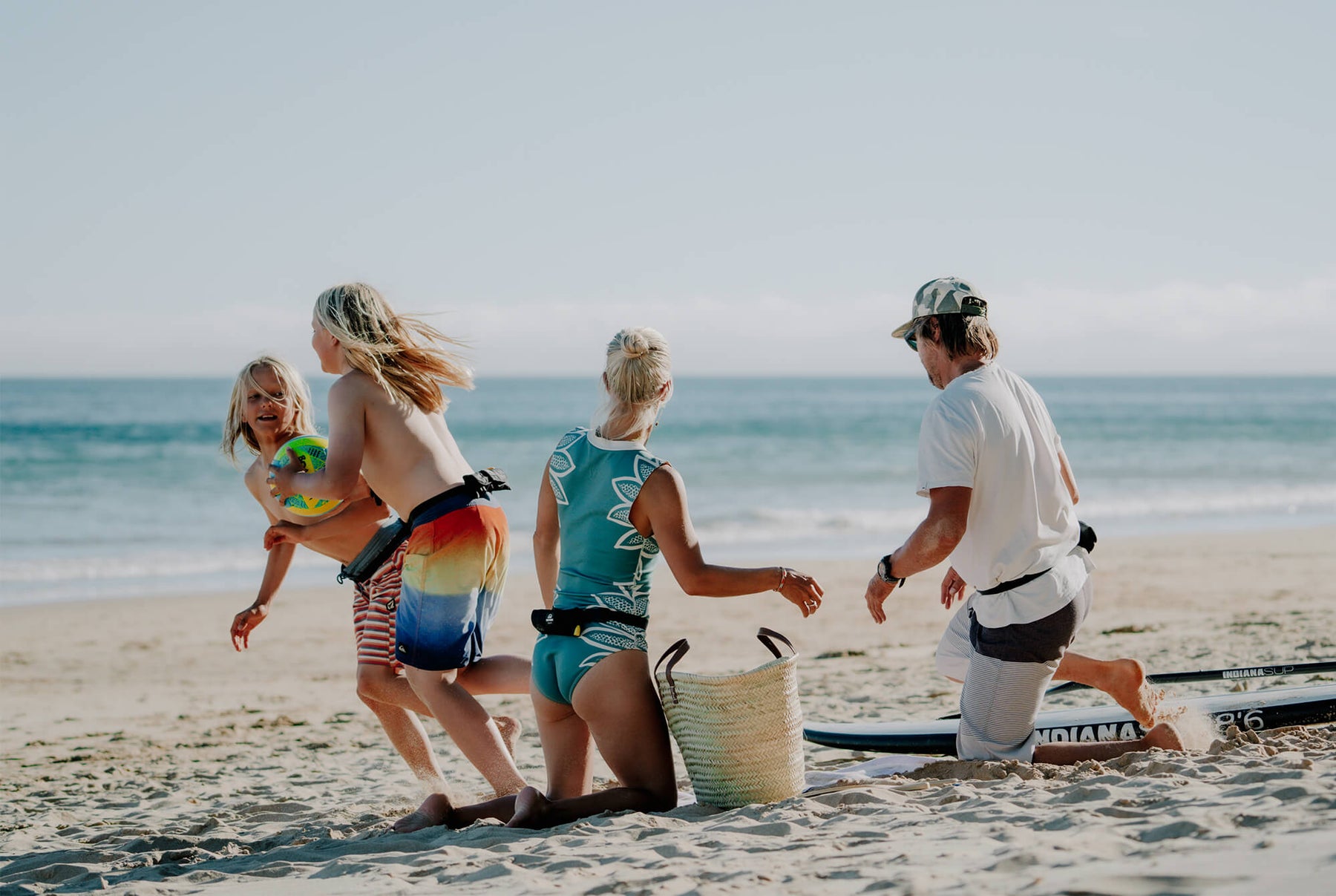 Familie mit getragenen Restube, Bord am Strand, Kinder schnappen sich einen Ball.