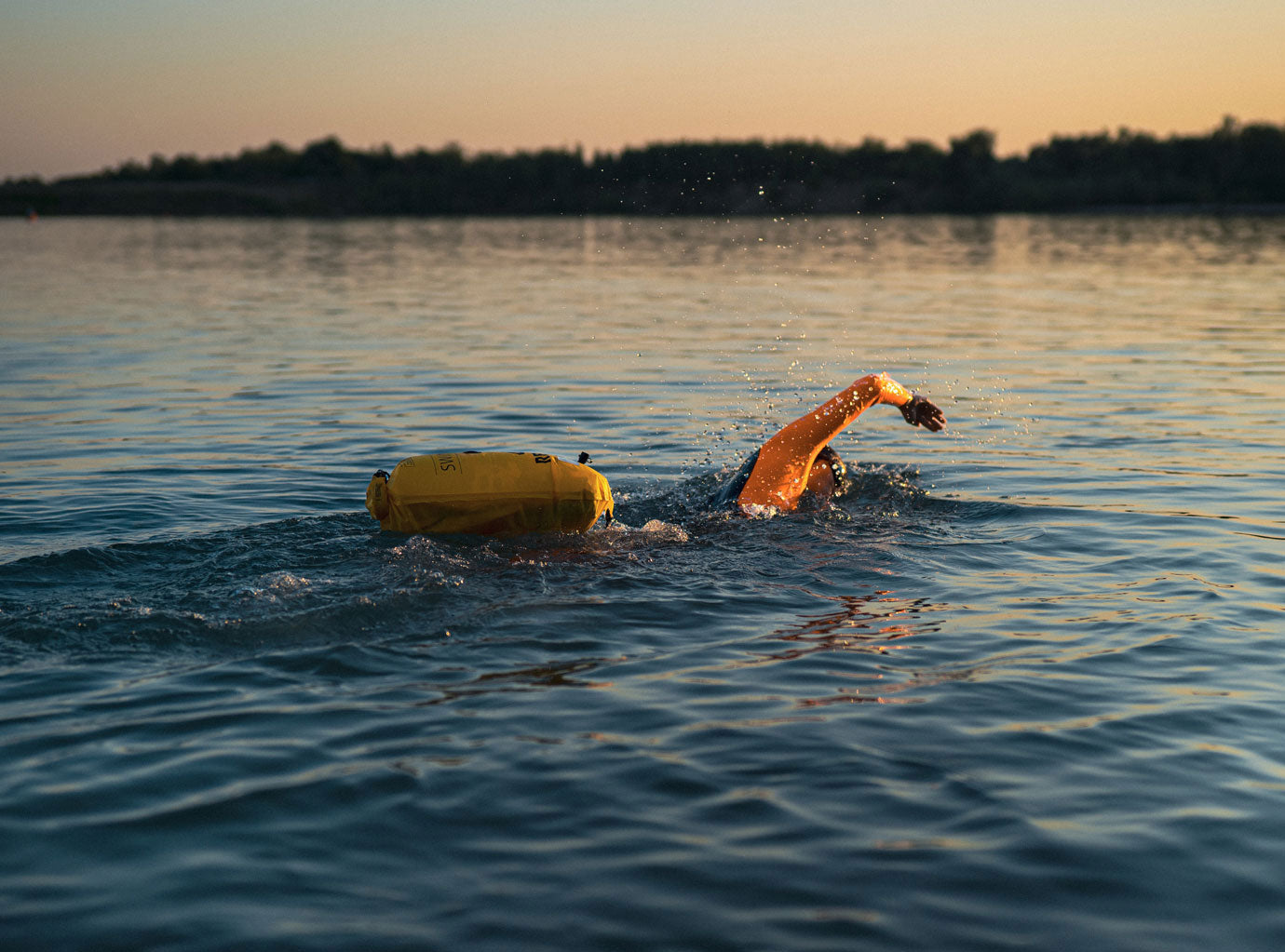 Woman swimming in a lake at sunset with the Swimbuoy by RESTUBE