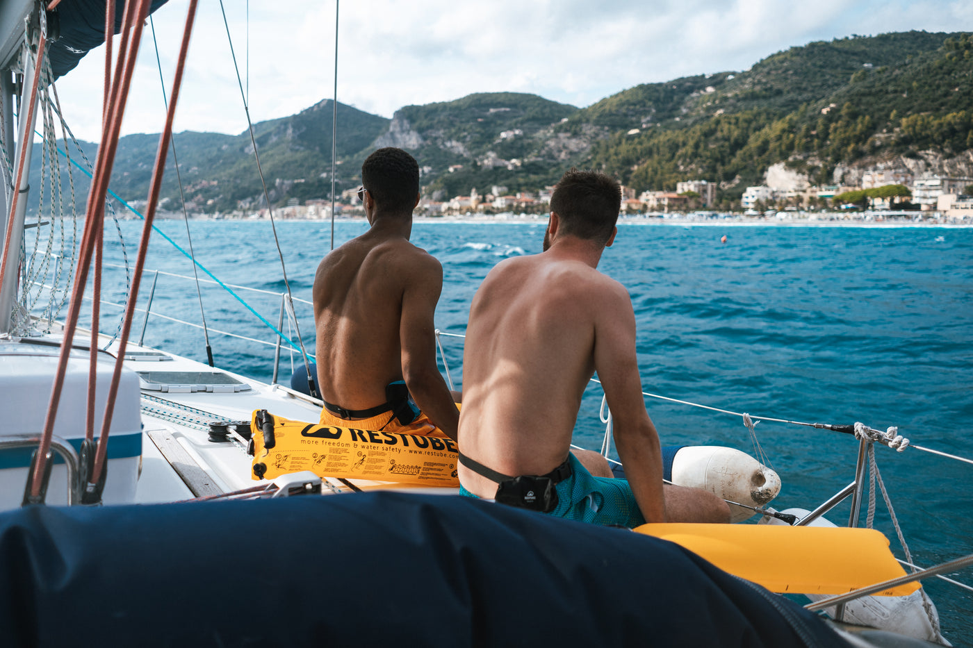 Zwei Männer sitzen auf einem Schiff an der Küste mit aufgeblasenen Restube Bojen und schauen auf das Meer. 