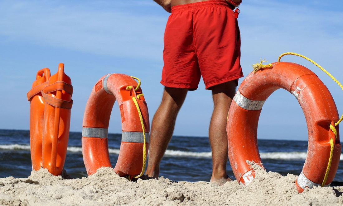 Rettungsschwimmer mit am Strand im Sand stehenden Rettungs-Bojen und -Ringen schaut übers Wasser.