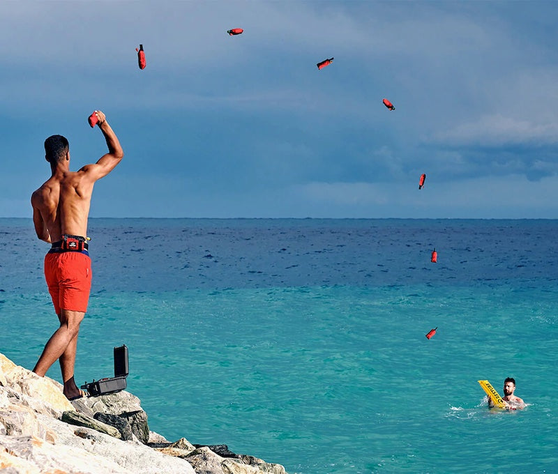 Rettungsschwimmer wirft vom Felsen aus eine Restube automatic zu einem Schwimmer im Meer