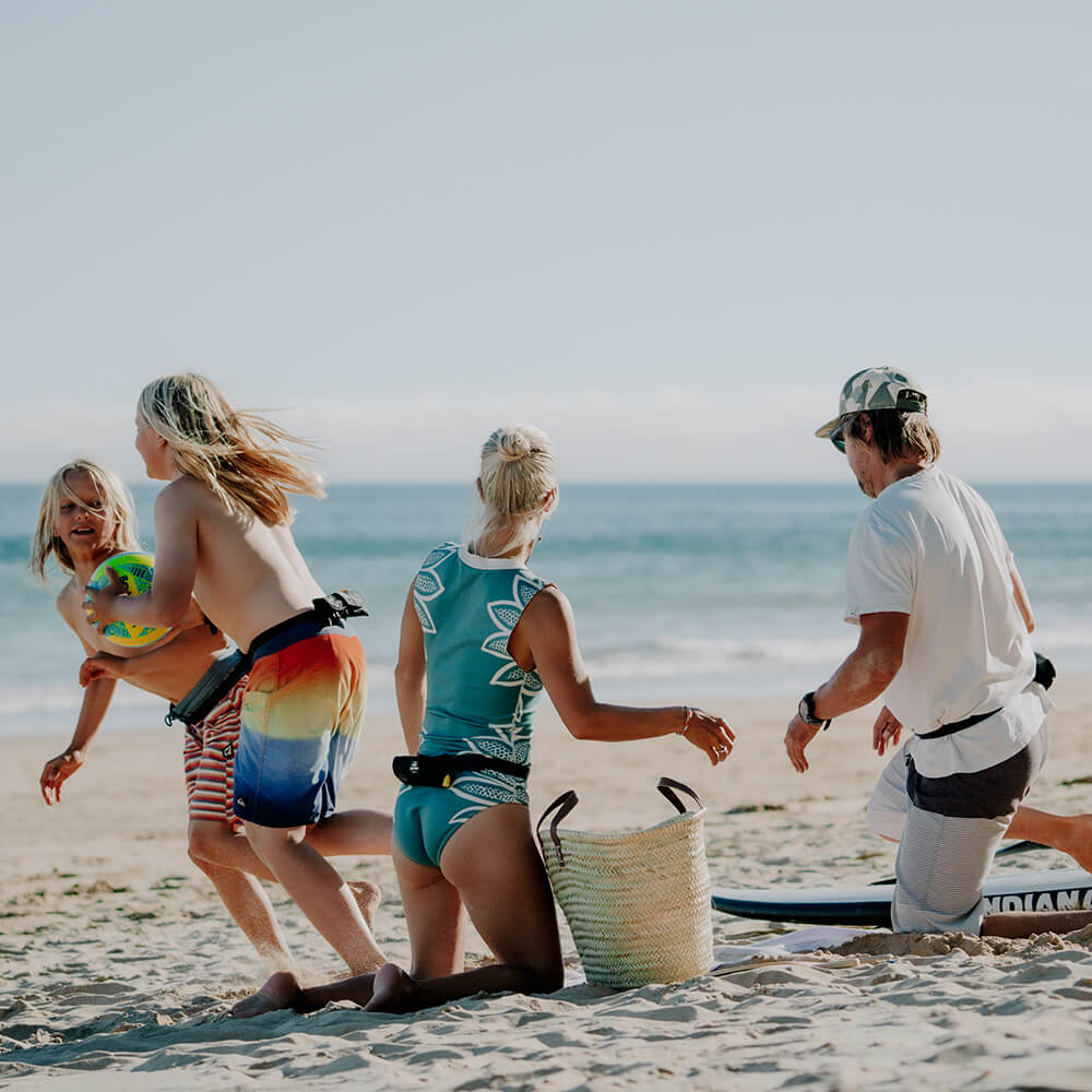 Familie mit Board und Restube am Sandstrand. Kinder rennen zu Ball spielen.